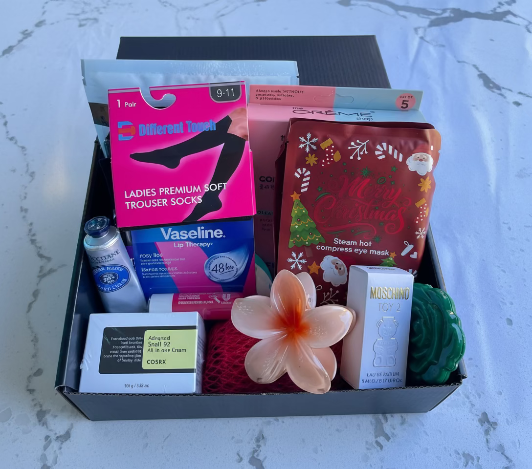 Assorted items including Vaseline rosy lip therapy, a flower claw, and other skin care /cosmetic products in a box on a marble surface.